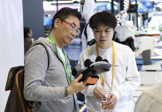 (251106) -- SHANGHAI, Nov. 6, 2025 (Xinhua) -- A visitor (L) learns about a wheeled exoskeleton product which made its global debut, at the Innovation Incubation Special Section during the 8th China International Import Expo (CIIE) in east China's Shanghai, Nov. 6, 2025. Many exhibitors debuted their latest products at the 8th CIIE in Shanghai. (Xinhua/Meng Chenguang)