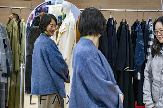 (251107) -- SHANGHAI, Nov. 7, 2025 (Xinhua) -- A visitor tries a wool coat from Mongolia at the Consumer Goods exhibition area of the eighth China International Import Expo (CIIE) in east China's Shanghai, Nov. 7, 2025. The eighth CIIE opened here on Wednesday. Enterprises from a total of 123 Belt and Road partner countries participated in this year's CIIE, increasing by 23.1 percent year on year. (Xinhua/Ding He)