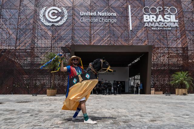(251107) -- BELEM(BRAZIL), Nov. 7, 2025 (Xinhua) -- A performer wearing traditional attire poses for a photo in front of the COP30 venue in Belem, Brazil, Nov. 6, 2025. UN Secretary-General Antonio Guterres and world leaders on Thursday urged governments to take immediate, decisive actions and make concerted efforts to combat climate change. (Xinhua/Wang Tiancong)