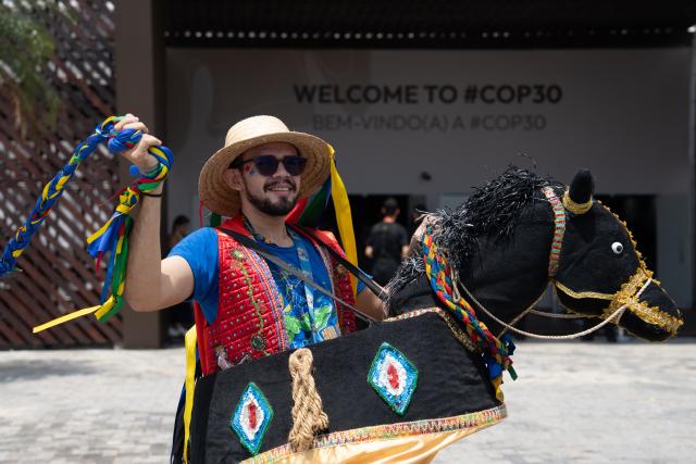(251107) -- BELEM(BRAZIL), Nov. 7, 2025 (Xinhua) -- A performer wearing traditional attire poses for a photo in front of the COP30 venue in Belem, Brazil, Nov. 6, 2025. UN Secretary-General Antonio Guterres and world leaders on Thursday urged governments to take immediate, decisive actions and make concerted efforts to combat climate change. (Xinhua/Wang Tiancong)