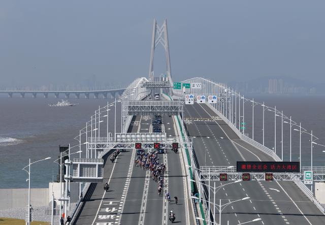 (251108) -- ZHUHAI, Nov. 8, 2025 (Xinhua) -- Athletes compete across the Hong Kong-Zhuhai-Macao Bridge during the men's road race of cycling road at China's 15th National Games in south China's Guangdong Province, Nov. 8, 2025. (Xinhua/Liang Xu)