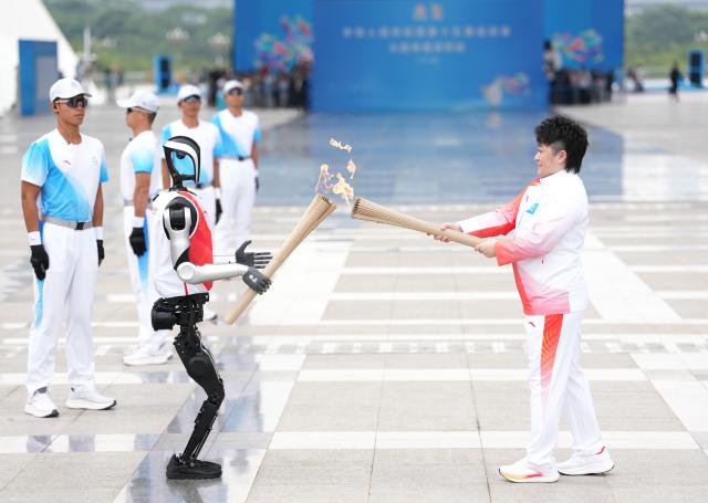 (251108) -- BEIJING, Nov. 8, 2025 (Xinhua) -- Torch bearer humanoid robot "Kuavo" (front) passes the flame during the torch relay for China's 15th National Games in Shenzhen, south China's Guangdong Province, Nov. 2, 2025. (Xinhua/Jiang Han)