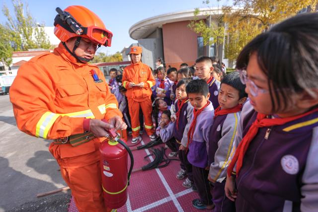 (251108) -- YINCHUAN, Nov. 8, 2025 (Xinhua) -- A staff member of Ningxia Helan Mountain National Nature Reserve Administration explains the use of fire extinguisher to students at a primary school in Yinchuan, northwest China's Ningxia Hui Autonomous Region, Nov. 7, 2025. Currently, the risk of forest fire is high across the Helan Mountain. Staff members of local nature reserve administration have rolled out a series of educational activities with the theme of forest fire prevention, aiming to enhance students' safety awareness via lectures, equipment demonstrations, and hands-on experiences. (Xinhua/Yang Zhisen)