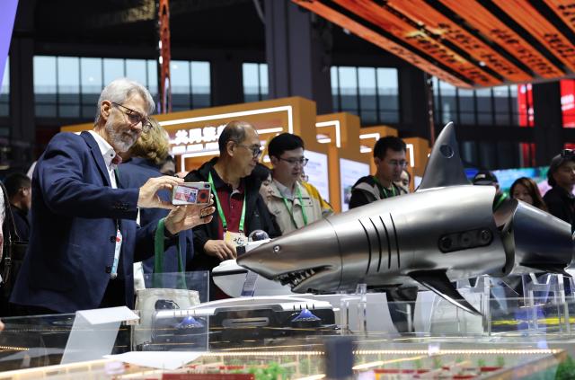 (251108) -- SHANGHAI, Nov. 8, 2025 (Xinhua) -- A guest takes photos of a bionic shark exhibited at the China Pavilion during the eighth China International Import Expo (CIIE) in east China's Shanghai, Nov. 8, 2025. Over 30 foreign talents and their families were invited to visit the eighth CIIE at the National Convention and Exhibition Center (Shanghai) during a themed event on Saturday. (Xinhua/Fang Zhe)