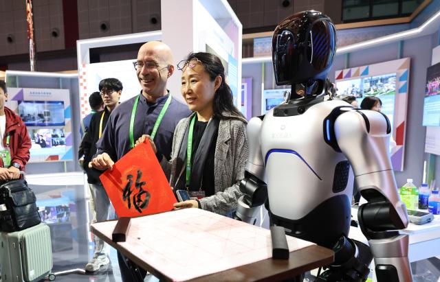 (251108) -- SHANGHAI, Nov. 8, 2025 (Xinhua) -- Guests hold a calligraphy written by a humanoid robot at the China Pavilion during the eighth China International Import Expo (CIIE) in east China's Shanghai, Nov. 8, 2025. Over 30 foreign talents and their families were invited to visit the eighth CIIE at the National Convention and Exhibition Center (Shanghai) during a themed event on Saturday. (Xinhua/Fang Zhe)