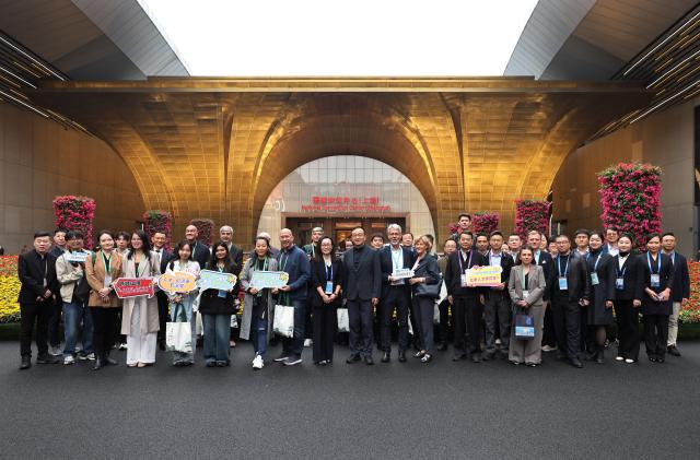 (251108) -- SHANGHAI, Nov. 8, 2025 (Xinhua) -- Guests pose for a group photo in front of the gate of the National Convention Center (Shanghai) during the eighth China International Import Expo (CIIE) in east China's Shanghai, Nov. 8, 2025. Over 30 foreign talents and their families were invited to visit the eighth CIIE at the National Convention and Exhibition Center (Shanghai) during a themed event on Saturday. (Xinhua/Fang Zhe)