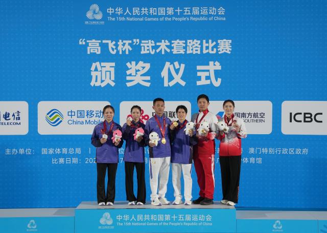 (251108) -- GUANGZHOU, Nov. 8, 2025 (Xinhua) -- Gold medalist Chen Huiying of Fujian, silver medalist Zhang Yaling of Fujian and bronze medalist He Aisang of Guangdong pose for photos with their coaches during the awarding ceremony for the women's Nanquan-Nandao-Nangun of Wushu Taolu event at China's 15th National Games in Guangzhou, south China's Guangdong Province, Nov. 8, 2025. (Xinhua/Jigme Dorji)
