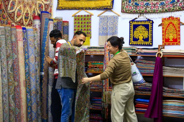 (251108) -- SHANGHAI, Nov. 8, 2025 (Xinhua) -- A visitor (R) learns about products at a carpet booth of Pakistan at the Consumer Goods Exhibition area during the eighth China International Import Expo (CIIE) in east China's Shanghai, Nov. 8, 2025. At the Consumer Goods Exhibition area of the eighth CIIE, apparel, daily chemicals, home furnishings, and cultural and sports products were prominently showcased, reflecting global consumption trends and improvements in quality of life. (Xinhua/Liu Jiaqi)