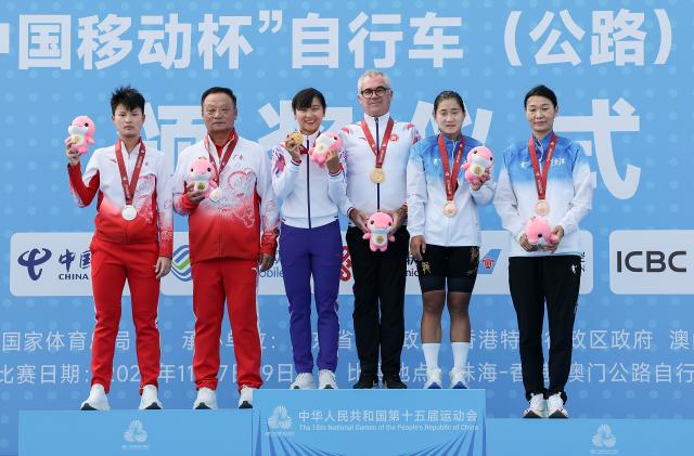 (251109) -- ZHUHAI, Nov. 9, 2025 (Xinhua) -- Gold medalist Lee Sze Wing (3rd L) of Hong Kong, silver medalist Wei Xiaoqing (1st L) of Guangdong, bronze medalist Feng Lin (2nd R) of Heilongjiang pose with their coaches during the awarding ceremony for the women's road race of cycling road at China's 15th National Games in south China's Guangdong Province, Nov. 9, 2025. (Xinhua/Mao Siqian)