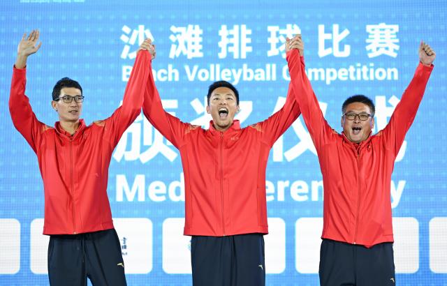 (251110) -- HONG KONG, Nov. 10, 2025 (Xinhua) -- Gold medalists Wu Jiaxin (L)/Zhou Chaowei (C) of Jiangsu and their coach greet the spectators during the awarding ceremony for the men's beach volleyball at China's 15th National Games in Hong Kong, south China, Nov. 10, 2025. (Xinhua/Hu Huhu)