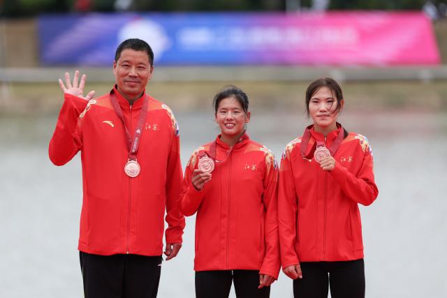 (251111) -- GUANGZHOU, Nov. 11, 2025 (Xinhua) -- Bronze medalists Wang Yuxin (C)/Liu Yuanyuan (R) of Jiangsu pose with their coach during the awarding ceremony after the women's double sculls final of rowing at China's 15th National Games in Guangzhou, south China's Guangdong Province, Nov. 11, 2025. (Xinhua/Pan Yulong)