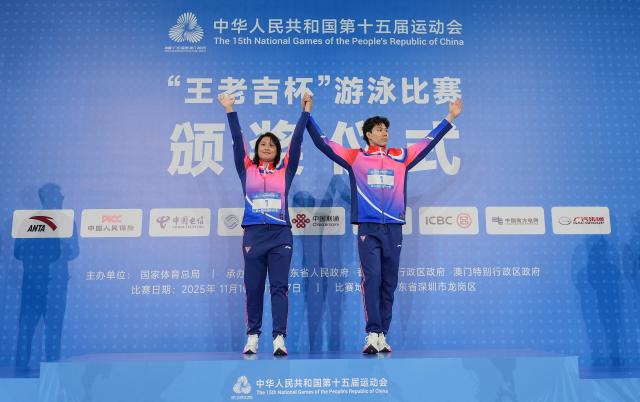 (251111) -- SHENZHEN, Nov. 11, 2025 (Xinhua) -- Gold medalist Qin Haiyang (R) of Shanghai and his coach are seen during the awarding ceremony after the men's 100m breaststroke final of swimming event at China's 15th National Games in Shenzhen, south China's Guangdong Province, Nov. 11, 2025. (Xinhua/Xia Yifang)