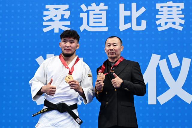 (251111) -- ZHAOQING, Nov. 11, 2025 (Xinhua) -- Gold medalist Qing Daga of Inner Mongolia poses with his coach during the awarding ceremony for Judo men's -73kg at China's 15th National Games in Zhaoqing, south China's Guangdong Province, Nov. 11, 2025. (Xinhua/Zhu Xiang)