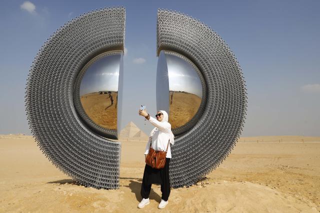 (251111) -- CAIRO, Nov. 11, 2025 (Xinhua) -- A visitor takes a selfie in front of an artwork exhibited during the "Forever Is Now" international art exhibition at Giza Pyramids scenic spot in Giza, Egypt, Nov. 11, 2025. The fifth edition of "Forever Is Now" international art exhibition on Tuesday kicked off in the area of Egypt's Giza Pyramids scenic spot, showcasing 10 artworks of artists from different countries. The exhibition runs from Nov. 11 to Dec. 6. (Xinhua/Ahmed Gomaa)