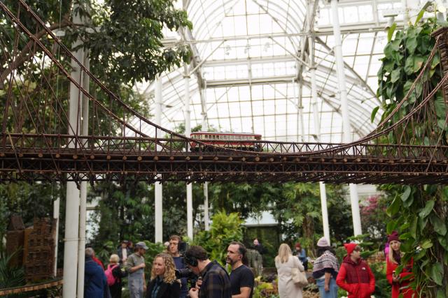 (251111) -- NEW YORK, Nov. 11, 2025 (Xinhua) -- Visitors are seen under a model of the Brooklyn Bridge during a preview of the Holiday Train Show at New York Botanical Garden in New York, the United States, on Nov. 11, 2025. A preview for the Holiday Train Show, which is open to the public from Nov. 15, 2025 to Jan. 11, 2026, was held at the New York Botanical Garden on Tuesday, showcasing large-scale model trains running in a miniature New York City where nearly 200 scaled iconic buildings and structures are recreated using bark, leaves and other natural materials. (Xinhua/Zhang Fengguo)