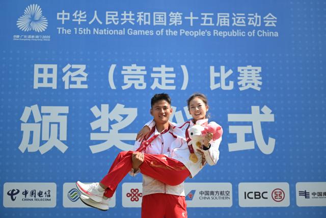 (251112) -- ZHUHAI, Nov. 12, 2025 (Xinhua) -- Gold medalist Yang Jiayu (R) of Beijing celebrates with her husband and coach Wei Xinmeng during the awarding ceremony for the women's 20km race walk of athletics at China's 15th National Games in Zhuhai, south China's Guangdong Province, Nov. 12, 2025. (Xinhua/Zhang Long)