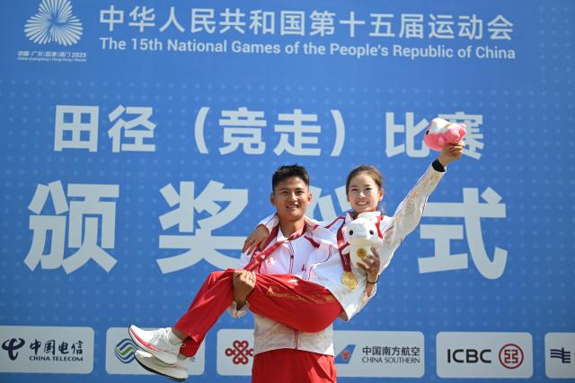 (251112) -- ZHUHAI, Nov. 12, 2025 (Xinhua) -- Gold medalist Yang Jiayu (R) of Beijing celebrates with her husband and coach Wei Xinmeng during the awarding ceremony for the women's 20km race walk of athletics at China's 15th National Games in Zhuhai, south China's Guangdong Province, Nov. 12, 2025. (Xinhua/Zhang Long)