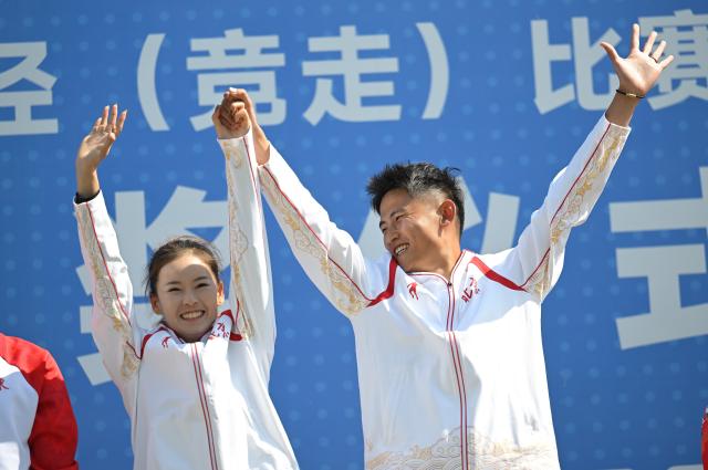 (251112) -- ZHUHAI, Nov. 12, 2025 (Xinhua) -- Gold medalist Yang Jiayu (L) of Beijing celebrates with her husband and coach Wei Xinmeng during the awarding ceremony for the women's 20km race walk of athletics at China's 15th National Games in Zhuhai, south China's Guangdong Province, Nov. 12, 2025. (Xinhua/Zhang Long)