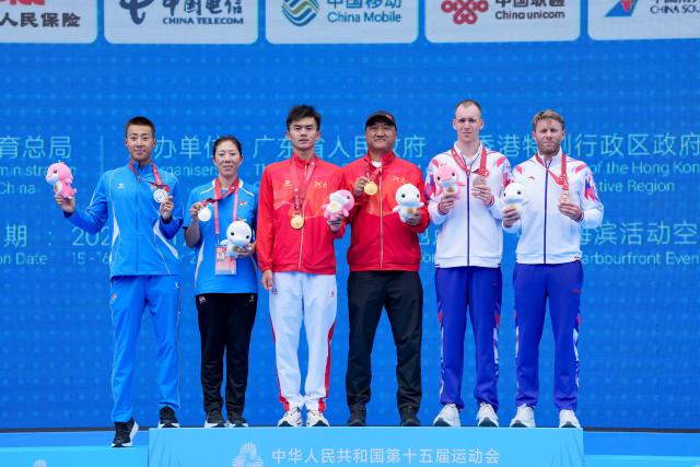 (251115) -- HONG KONG, Nov. 15, 2025 (Xinhua) -- Gold medalist Fan Junjie (3rd L) of Henan, silver medalist Chen Qi (1st L) of Liaoning, bronze medalist Oscar Coggins (2nd R) of Hong Kong pose with their coaches during the awarding ceremony for the men's individual triathlon at China's 15th National Games in Hong Kong, south China, Nov. 15, 2025. (Xinhua/Wu Lu)