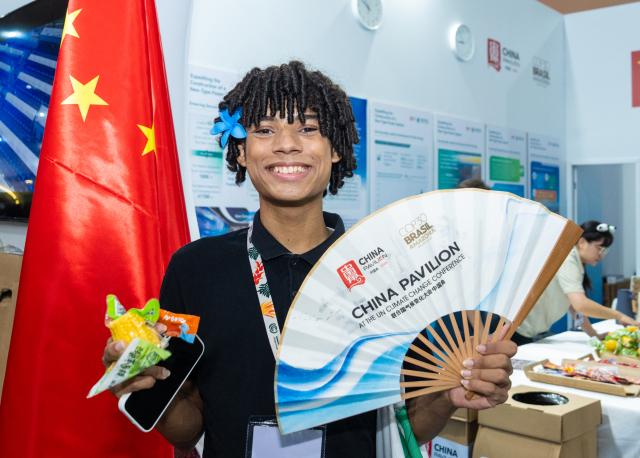 (251115) -- BELEM, Nov. 15, 2025 (Xinhua) -- A guest displays a folding fan at the China Pavilion during the 30th United Nations climate change conference in Belem, Brazil, Nov. 12, 2025. The 30th United Nations climate change conference, commonly known as COP30, opened Monday in Belem, Brazil. Displays of Chinese cultural products, green technologies, and innovations attracted attention of the attendees during the conference. (Xinhua/Wang Tiancong)