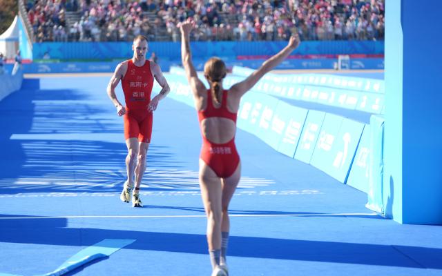 (251116) -- HONG KONG, Nov. 16, 2025 (Xinhua) -- Oscar Coggins (L) of Hong Kong crosses the finish line during the triathlon mixed relay at China's 15th National Games in Hong Kong, south China, Nov. 16, 2025. (Xinhua/Lui Sui Wai)