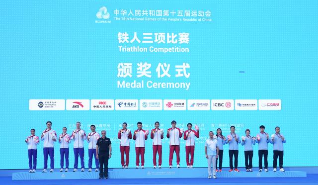 (251116) -- HONG KONG, Nov. 16, 2025 (Xinhua) -- Gold medalists team Shandong (C), silver medalists team Hong Kong (L) and bronze medalists team Gongan pose during the awarding ceremony for the triathlon mixed relay at China's 15th National Games in Hong Kong, south China, Nov. 16, 2025. (Xinhua/Lui Sui Wai)