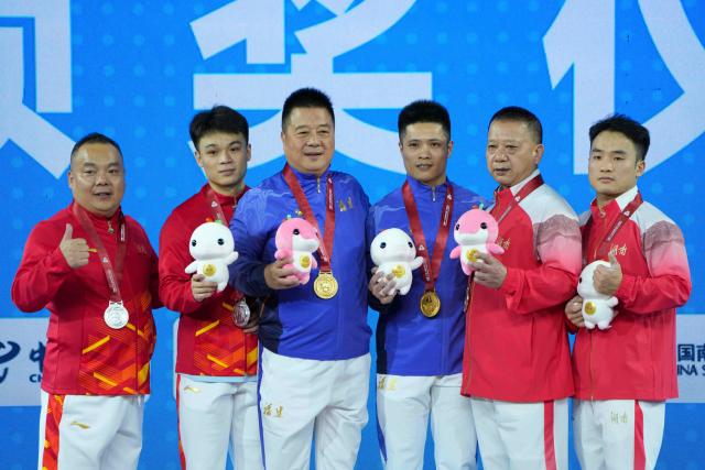 (251116) -- BEIJING, Nov. 16, 2025 (Xinhua) -- Gold medalist Li Fabin of Fujian, silver medalist Ding Hongjie of Chongqing and bronze medalist Qu Hongcheng of Hunan pose with their coaches during the awarding ceremony after the weightlifting men's 61kg final at China's 15th National Games in Dongguan, south China's Guangdong Province, Nov. 16, 2025. (Xinhua/Yang Chenguang)