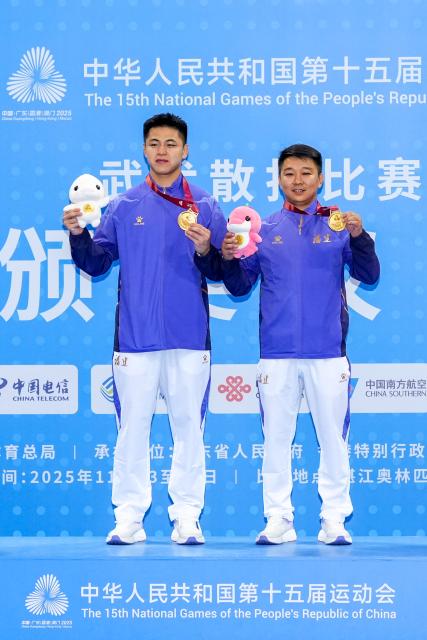 (251116) -- ZHANJIANG, Nov. 16, 2025 (Xinhua) -- Gold medalist Lin Hongwei of Fujian poses with his coach Zhao Xiaorui during the awarding ceremony for wushu sanda men's 75kg at China's 15th National Games in Zhanjiang, south China's Guangdong Province, Nov. 16, 2025. (Xinhua/Li Bo)