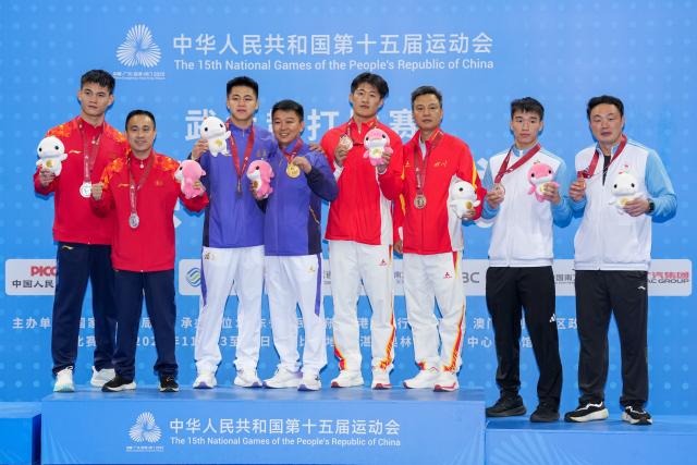 (251116) -- ZHANJIANG, Nov. 16, 2025 (Xinhua) -- Gold medalist Lin Hongwei of Fujian, silver medalist He Feng of Chongqing, along with bronze medalists Lu Haitao of Sichuan and Jin Gensheng of Beijing Sport University pose with their coaches during the awarding ceremony for wushu sanda men's 75kg at China's 15th National Games in Zhanjiang, south China's Guangdong Province, Nov. 16, 2025. (Xinhua/Li Bo)
