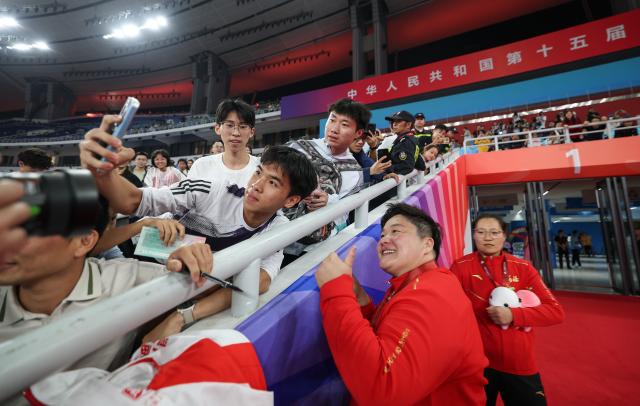 (251116) -- GUANGZHOU, Nov. 16, 2025 (Xinhua) -- Gold medalist Gong Lijiao (R front) of Hebei pose for a selfie with the spectators after the awarding ceremony for the women's shot put of athletics at China's 15th National Games in Guangzhou, south China's Guangdong Province, Nov. 16, 2025. (Xinhua/Huang Wei)