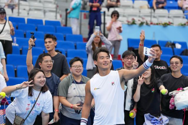 (251117) -- HENGQIN, Nov. 17, 2025 (Xinhua) -- Bu Yunchaokete (front) takes selfies with the fans after the men's singles third round match of tennis between Bu Yunchaokete of Zhejiang and Wang Aoran of Tianjin at China's 15th National Games in Hengqin, south China's Guangdong Province, Nov. 17, 2025. (Xinhua/Yan Linyun)