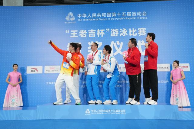 (251117) -- SHENZHEN, Nov. 17, 2025 (Xinhua) -- Gold medalist Xu Jiayu of Zhejiang, silver medalist Wang Zicheng of Hubei and bronze medalist Jiang Chenglin of Shaanxi pose for a selfie with their coaches during the awarding ceremony for the men's 50m backstroke of swimming at China's 15th National Games in Shenzhen, south China's Guangdong Province, Nov. 17, 2025. (Xinhua/Xue Yuge)