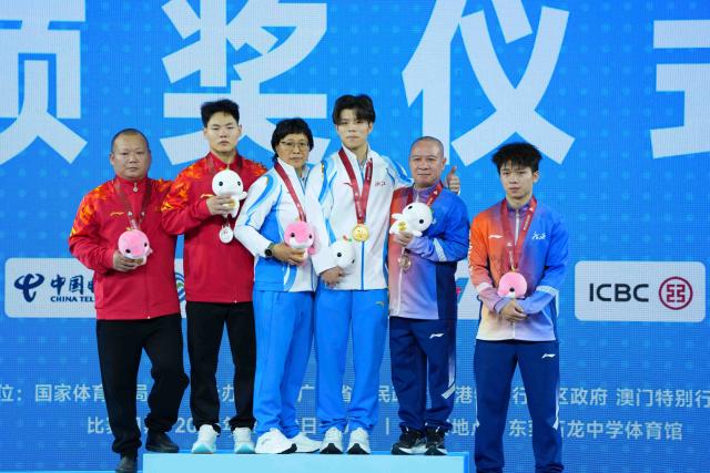 (251117) -- DONGGUAN, Nov. 17, 2025 (Xinhua) -- Gold medalist Chen Jian of Zhejiang, silver medalist Cheng Jun of Chongqing and bronze medalist Zhong Yuanlong of Guangxi pose with their coaches during the awarding ceremony for weightlifting men's 67kg at China's 15th National Games in Dongguan, south China's Guangdong Province, Nov. 17, 2025. (Xinhua/Yang Chenguang)