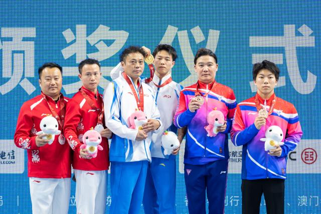 (251117) -- ZHAOQING, Nov. 17, 2025 (Xinhua) -- Gold medalist Chen Yilu of Zhejiang, silver medalist Chen Zhilong of Guizhou and bronze medalist Zhang Zhishan of Shanghai pose with their coaches during the awarding ceremony for the artistic gymnastics men's vault at China's 15th National Games in Zhaoqing, south China's Guangdong Province, Nov. 17, 2025. (Xinhua/Du Zixuan)