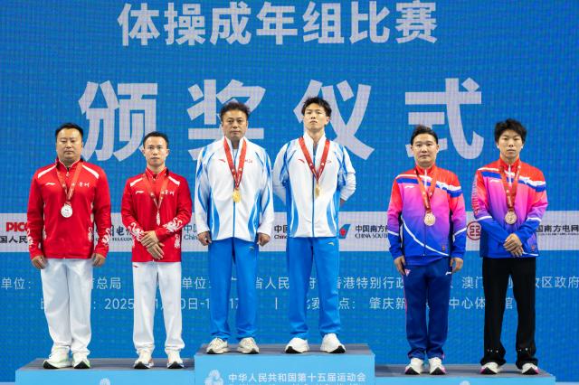 (251117) -- ZHAOQING, Nov. 17, 2025 (Xinhua) -- Gold medalist Chen Yilu of Zhejiang, silver medalist Chen Zhilong of Guizhou and bronze medalist Zhang Zhishan of Shanghai pose with their coaches during the awarding ceremony for the artistic gymnastics men's vault at China's 15th National Games in Zhaoqing, south China's Guangdong Province, Nov. 17, 2025. (Xinhua/Du Zixuan)