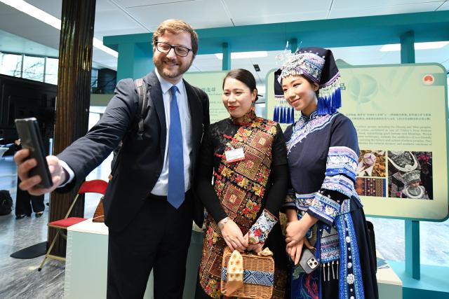 (251118) -- GENEVA, Nov. 18, 2025 (Xinhua) -- A visitor (L) takes selfies with staff members in Chinese folk costumes during China (Guangxi) Geographical Indication Products Exhibition at the World Intellectual Property Organization (WIPO) headquarters in Geneva, Switzerland, Nov. 17, 2025.
  The two-day exhibition kicked off here on Monday, showcasing iconic products from south China's Guangxi Zhuang Autonomous Region, including tea, pottery and bamboo weaving craft. (Xinhua/Lian Yi)