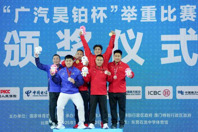 (251119) -- DONGGUAN, Nov. 19, 2025 (Xinhua) -- Gold medalist Qian Feixiang of Jiangsu, silver medalist Zhao Yongchao of Fujian and bronze medalist Liu Xinxin of Shaanxi pose with their coaches during the awarding ceremony after the weightlifting men's 96kg final at China's 15th National Games in Dongguan, south China's Guangdong Province, Nov. 19, 2025. (Xinhua/Yang Chenguang)