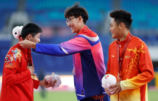 (251119) -- GUANGZHOU, Nov. 19, 2025 (Xinhua) -- Gold medalist Xu Zhuoyi (C) of Shanghai, silver medalist Liu Junxi (L) of Jiangsu and bronze medalist Zhu Shenglong of Hubei react during the awarding ceremony for the men's 110m hurdles of athletics at China's 15th National Games in Guangzhou, south China's Guangdong Province, Nov. 19, 2025. (Xinhua/Huang Wei)