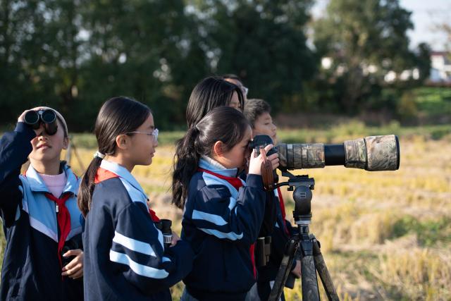 (251120) -- CHIZHOU, Nov. 20, 2025 (Xinhua) -- Students of Maotan Primary School record birds with a camera under the guidance of a wild bird conservation volunteer at the Shibasuo provincial nature reserve in Chizhou City, east China's Anhui Province, Nov. 18, 2025.
  Maotan Primary School is adjacent to the Shibasuo provincial nature reserve. The reserve boasts abundant wildlife resources and protects mainly wintering waterfowl such as storks and geese, as well as the wetland ecosystem. It serves as a unique "nature classroom" for the school, especially in wetland conservation education.
  For years, the school has integrated wetland protection education into its daily teaching. Volunteers are invited to the school for wetland science popularization, and students are frequently organized for study tours in the wetlands. This teaching approach has deepened the children's understanding of wetland conservation. (Xinhua/Zhang Duan)