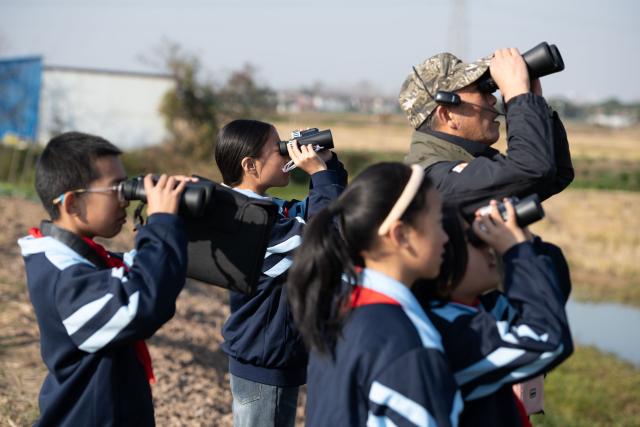 (251120) -- CHIZHOU, Nov. 20, 2025 (Xinhua) -- Students of Maotan Primary School observe birds under the guidance of a wild bird conservation volunteer at the Shibasuo provincial nature reserve in Chizhou City, east China's Anhui Province, Nov. 18, 2025.
  Maotan Primary School is adjacent to the Shibasuo provincial nature reserve. The reserve boasts abundant wildlife resources and protects mainly wintering waterfowl such as storks and geese, as well as the wetland ecosystem. It serves as a unique "nature classroom" for the school, especially in wetland conservation education.
  For years, the school has integrated wetland protection education into its daily teaching. Volunteers are invited to the school for wetland science popularization, and students are frequently organized for study tours in the wetlands. This teaching approach has deepened the children's understanding of wetland conservation. (Xinhua/Zhang Duan)