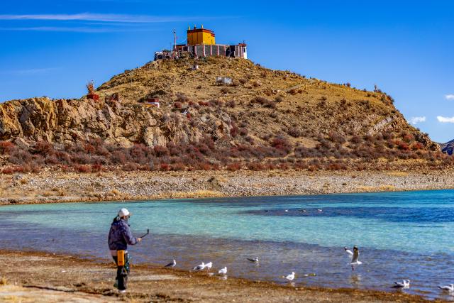 (251121) -- LHASA, Nov. 21, 2025 (Xinhua) -- A tourist takes photos at the Yamzbog Yumco Lake in southwest China's Xizang Autonomous Region on Nov. 20, 2025. (Xinhua/Jiang Fan)