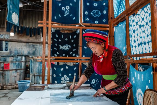 (251122) -- DALI, Nov. 22, 2025 (Xinhua) -- Duan Yinmei, an inheritor of the tie-dye technique of Bai ethnic group, dyes patterns on fabrics in a dyehouse in Zhoucheng Village of Dali Bai Autonomous Prefecture, southwest China's Yunnan Province, Nov. 21, 2025. Known as the hometown of the tie-dye technique of Bai ethnic group, Zhoucheng Village hosts over 200 households engaging in tie-dye businesses, with the number of employees exceeding 4,000. 
  As a traditional folk technique of the Bai ethnic group, tie-dye boasts a history spanning over a thousand years and was included in the first batch of China's national intangible cultural heritage list in 2006. Tying and dyeing are the core steps in the process of making indigo tie-dye products. Artisans use needles and threads to create various patterns on the fabric, which are then dyed with plant-based dyes, resulting in blue backgrounds adorned with vivid white patterns. (Xinhua/Hu Chao)