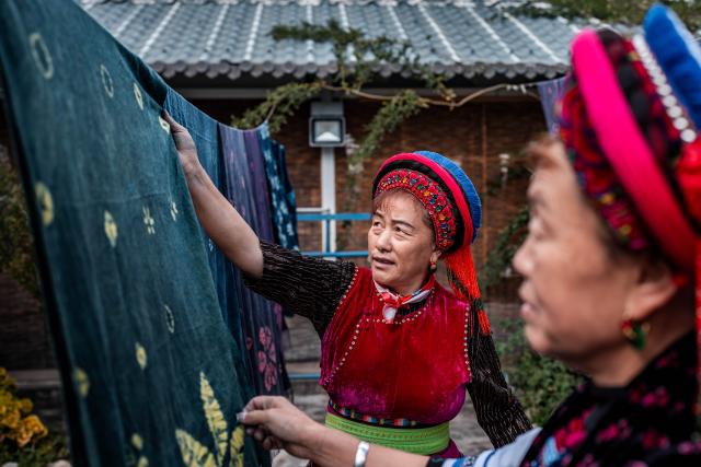 (251122) -- DALI, Nov. 22, 2025 (Xinhua) -- Duan Yinmei (L), an inheritor of the tie-dye technique of Bai ethnic group, and handicraftsman Duan Lilan dry tie-dye fabrics in a dyehouse in Zhoucheng Village of Dali Bai Autonomous Prefecture, southwest China's Yunnan Province, Nov. 21, 2025. Known as the hometown of the tie-dye technique of Bai ethnic group, Zhoucheng Village hosts over 200 households engaging in tie-dye businesses, with the number of employees exceeding 4,000. 
  As a traditional folk technique of the Bai ethnic group, tie-dye boasts a history spanning over a thousand years and was included in the first batch of China's national intangible cultural heritage list in 2006. Tying and dyeing are the core steps in the process of making indigo tie-dye products. Artisans use needles and threads to create various patterns on the fabric, which are then dyed with plant-based dyes, resulting in blue backgrounds adorned with vivid white patterns. (Xinhua/Hu Chao)