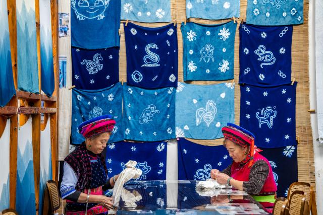 (251122) -- DALI, Nov. 22, 2025 (Xinhua) -- Duan Yinmei (R), an inheritor of the tie-dye technique of Bai ethnic group, and handicraftsman Duan Lilan create knots on fabrics in a dyehouse in Zhoucheng Village of Dali Bai Autonomous Prefecture, southwest China's Yunnan Province, Nov. 21, 2025. Known as the hometown of the tie-dye technique of Bai ethnic group, Zhoucheng Village hosts over 200 households engaging in tie-dye businesses, with the number of employees exceeding 4,000. 
  As a traditional folk technique of the Bai ethnic group, tie-dye boasts a history spanning over a thousand years and was included in the first batch of China's national intangible cultural heritage list in 2006. Tying and dyeing are the core steps in the process of making indigo tie-dye products. Artisans use needles and threads to create various patterns on the fabric, which are then dyed with plant-based dyes, resulting in blue backgrounds adorned with vivid white patterns. (Xinhua/Hu Chao)