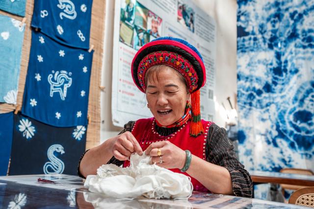 (251122) -- DALI, Nov. 22, 2025 (Xinhua) -- Duan Yinmei, an inheritor of the tie-dye technique of Bai ethnic group, creates knots on fabrics in a dyehouse in Zhoucheng Village of Dali Bai Autonomous Prefecture, southwest China's Yunnan Province, Nov. 21, 2025. Known as the hometown of the tie-dye technique of Bai ethnic group, Zhoucheng Village hosts over 200 households engaging in tie-dye businesses, with the number of employees exceeding 4,000. 
  As a traditional folk technique of the Bai ethnic group, tie-dye boasts a history spanning over a thousand years and was included in the first batch of China's national intangible cultural heritage list in 2006. Tying and dyeing are the core steps in the process of making indigo tie-dye products. Artisans use needles and threads to create various patterns on the fabric, which are then dyed with plant-based dyes, resulting in blue backgrounds adorned with vivid white patterns. (Xinhua/Hu Chao)