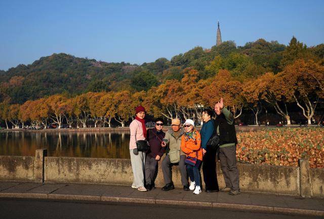 (251123) -- HANGZHOU, Nov. 23, 2025 (Xinhua) -- Tourists pose for photos at the West Lake scenic area in Hangzhou, east China's Zhejiang Province, Nov. 23, 2025.
  The weather in Hangzhou has been fine in recent days. Many tourists get up early in the morning to visit West Lake and enjoy the beautiful winter scenery here. (Xinhua/Han Chuanhao)