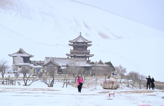 (251123) -- DUNHUANG, Nov. 23, 2025 (Xinhua) -- Tourists visit the Mingsha Mountain and Crescent Spring Scenic Area in Dunhuang City, northwest China's Gansu Province, on Nov. 23, 2025. Covered in a blanket of snow, the well-known tourist attractions in Dunhuang presented a stunning winter landscape. (Photo by Zhang Xiaoliang/Xinhua)