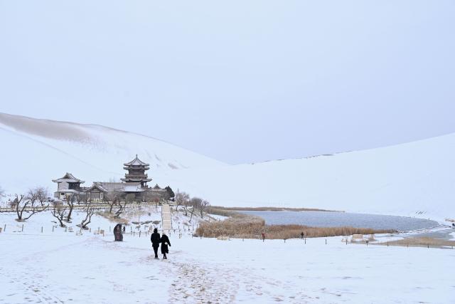 (251124) -- BEIJING, Nov. 24, 2025 (Xinhua) -- Tourists visit the Mingsha Mountain and Crescent Spring Scenic Area in Dunhuang City, northwest China's Gansu Province, on Nov. 23, 2025. Covered in a blanket of snow, the well-known tourist attractions in Dunhuang presented a stunning winter landscape. (Photo by Zhang Xiaoliang/Xinhua)