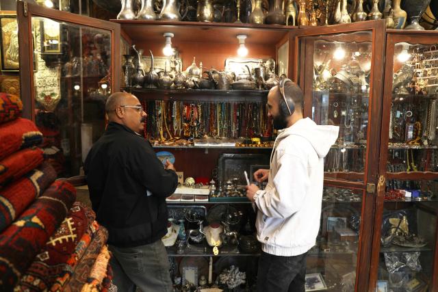 (251124) -- BAGHDAD, Nov. 24, 2025 (Xinhua) -- The owner of an antique shop displays his collections to a customer in a local culture market in Baghdad, Iraq, Nov. 24, 2025. (Xinhua/Khalil Dawood)