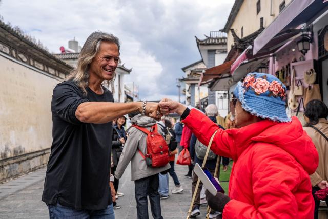 (251125) -- DALI, Nov. 25, 2025 (Xinhua) -- Brian Linden (L), an American living in Xizhou old town, bumps fists with a Singaporean tourist in Dali City, southwest China's Yunnan Province, Nov. 24, 2025. (Xinhua/Hu Chao)